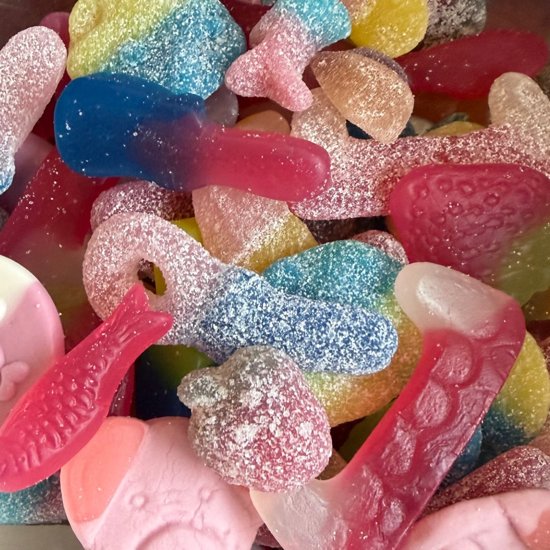 A close-up pile of colorful gummy candies and soft gummy shapes coated with white sugar powder, including pink, blue, yellow, red, and peach tones., assorted vegan gummy shapes and sour sweet
